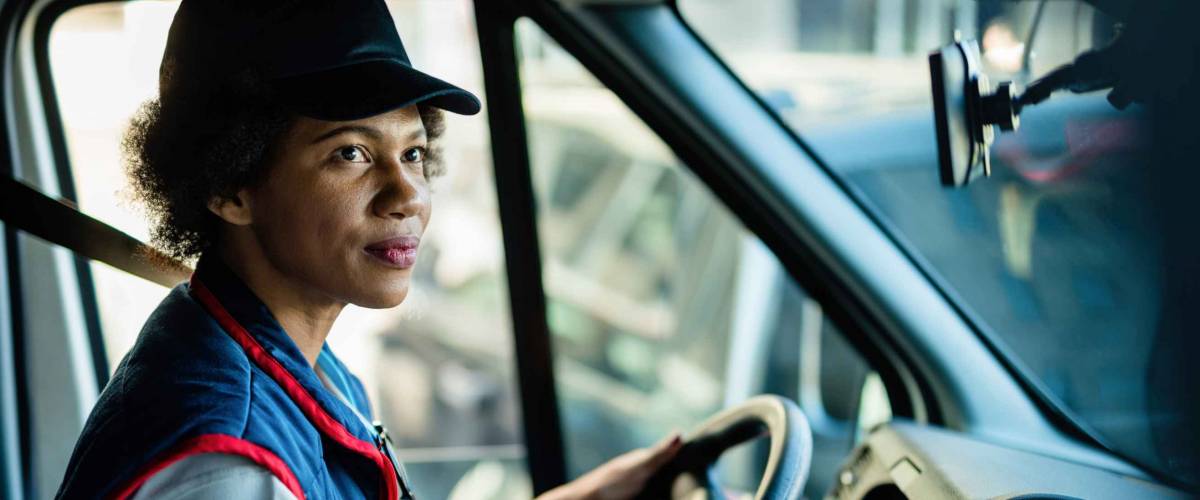 African American female courier driving delivery van in the city.