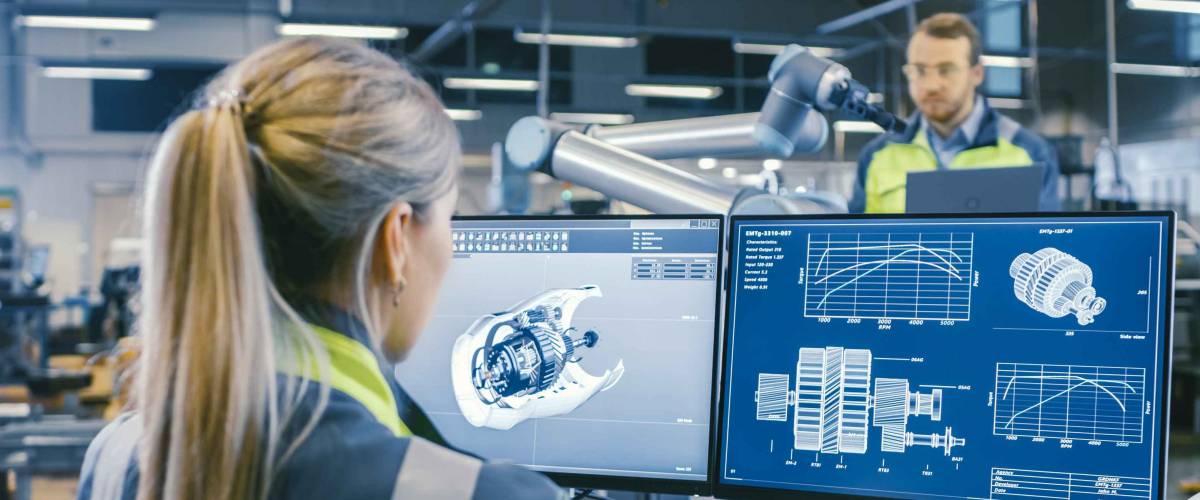 At the Factory: Female Mechanical Engineer Designs 3D Engine on Her Personal Computer. In the Background Male Automation Engineer who Uses Laptop for Programming Robotic Arm.