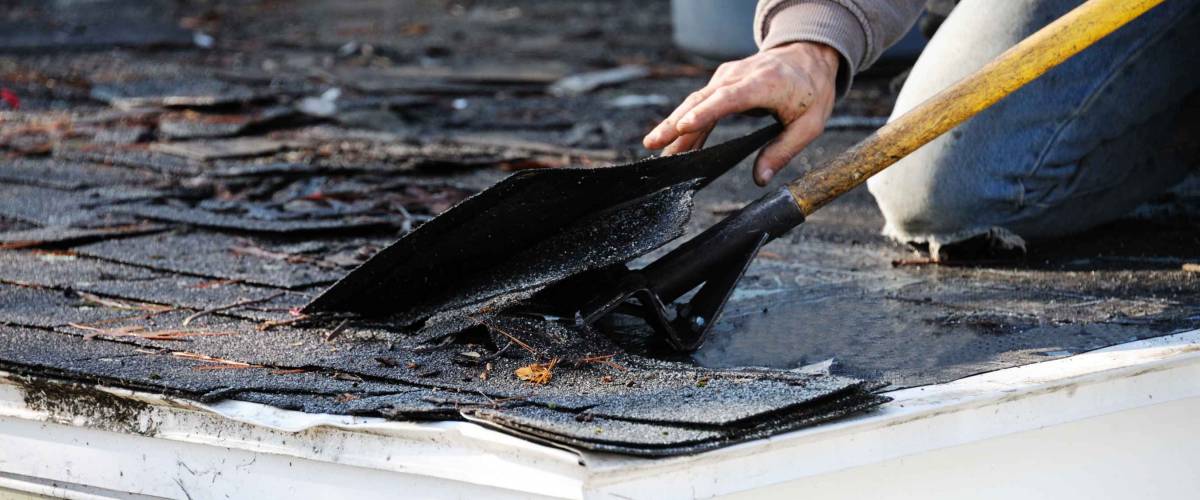 Person using a tool to remove shingles on a house