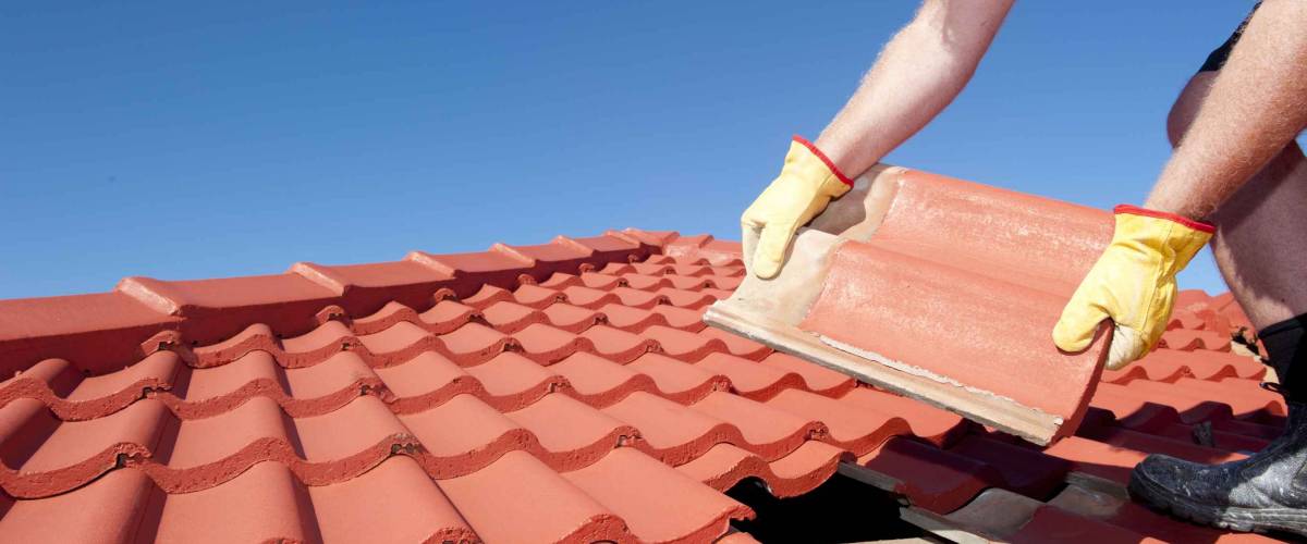 Hands wearing gloves laying tiles on a roof