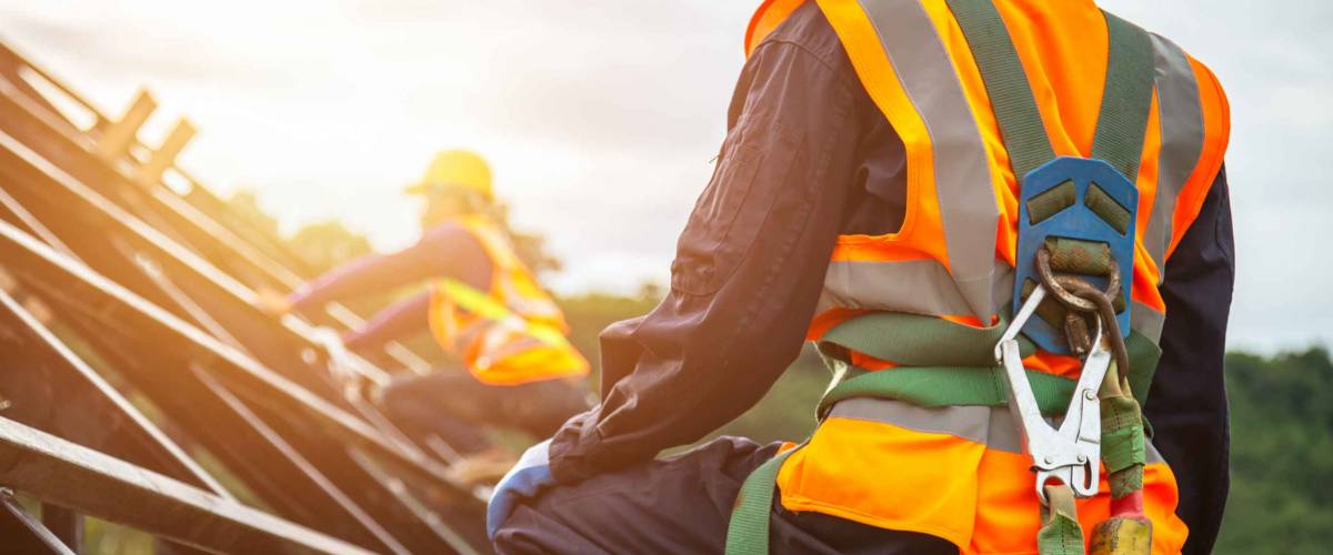 Two workers on a roof wearing safety equipment