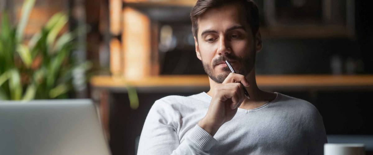 Man holding pen to his lip and looking thoughtful