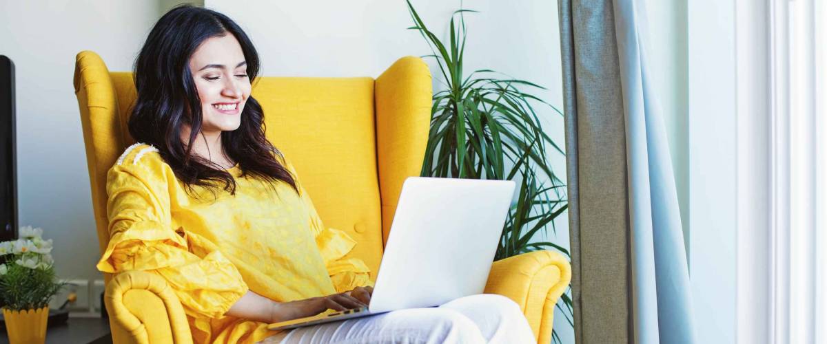 Young woman using laptop in yellow wingback chair