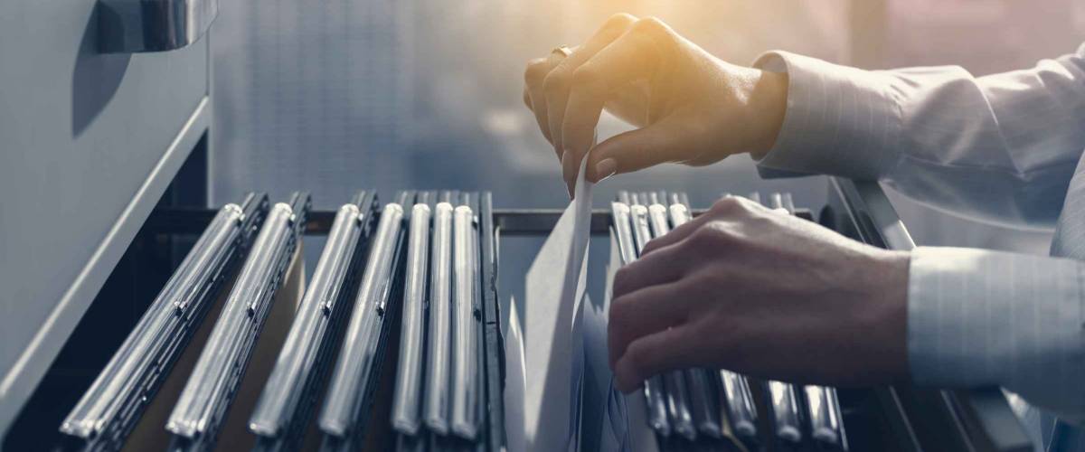 Professional female office clerk searching files and paperwork in the filing cabinet