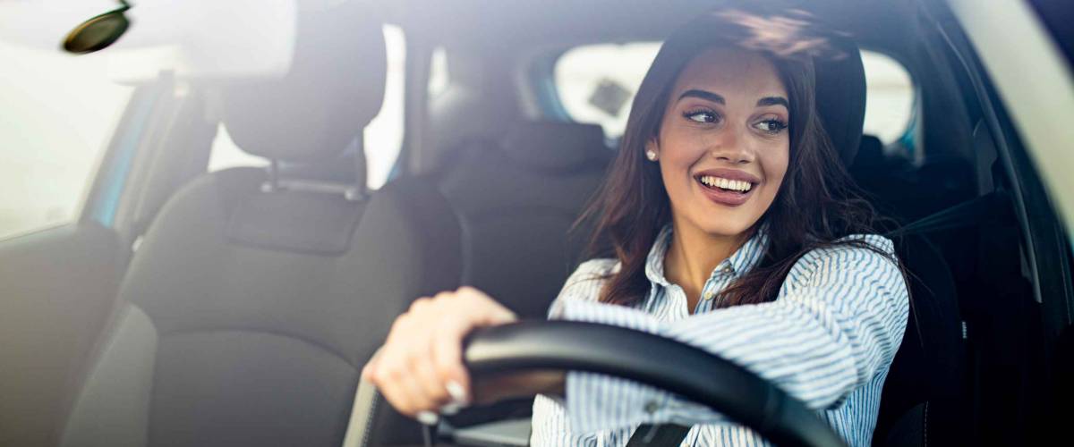 Happy woman driving a car and smiling. Cute young success happy brunette woman is driving a car. Portrait of happy female driver steering car with safety belt
