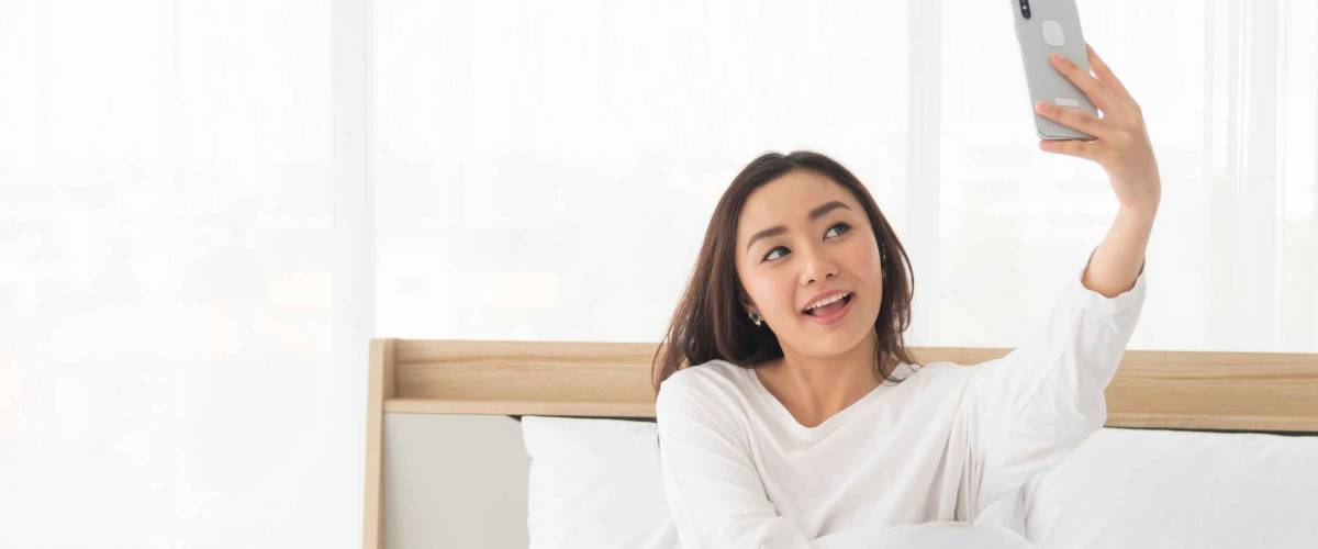 Happy young woman smiling in bed, talking to phone