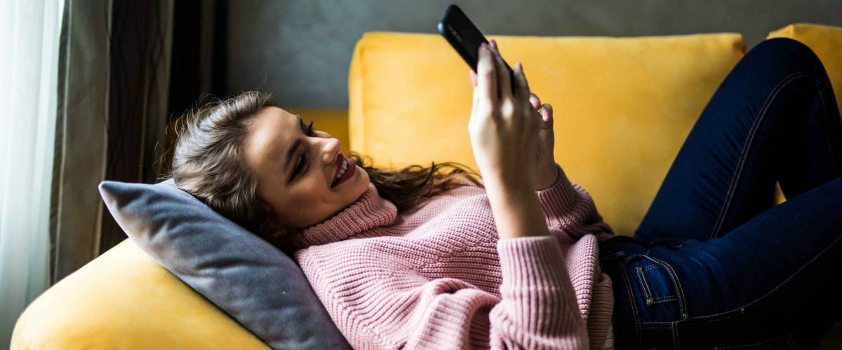 young woman relaxing on bright yellow couch, looking at phone