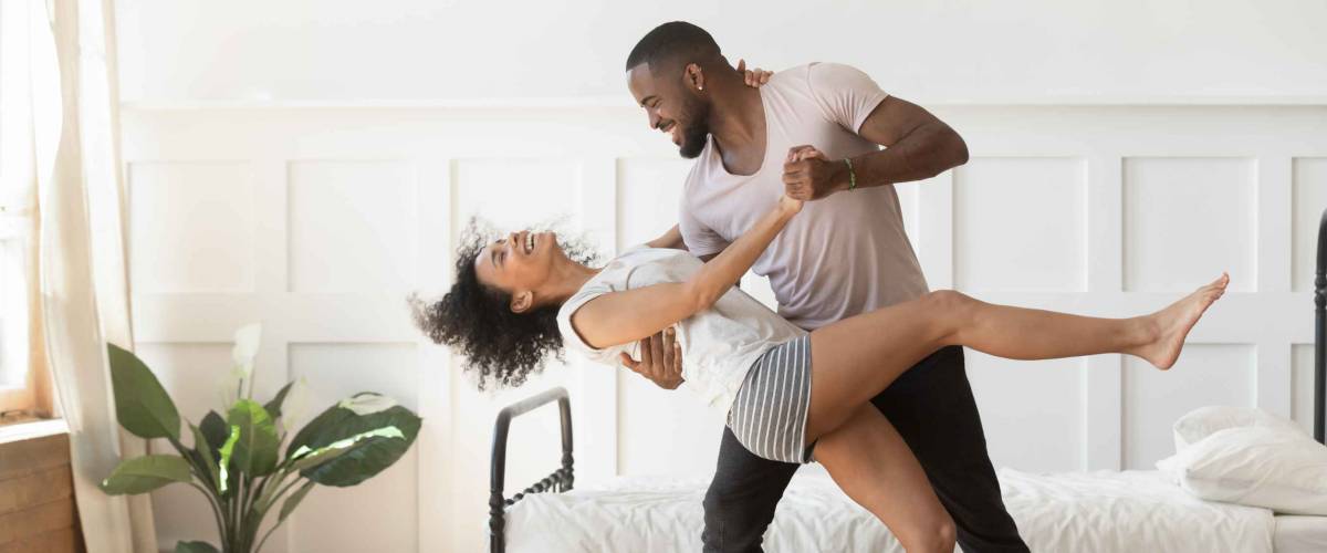Cheerful active romantic couple wearing pajamas dancing in bedroom together,