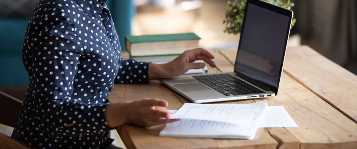 Young woman sitting at desk, using laptop and looking through papers