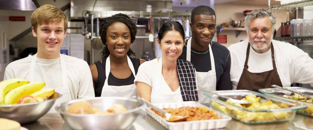 Young people pose and smile in industrial kitchen with older man