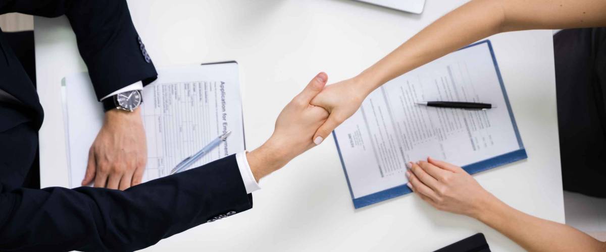 Two women shaking hands across a desk, shot from above