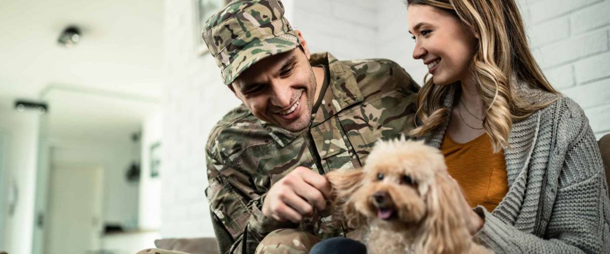 Young happy military officer having fun with his wife and dog after coming home from an assignment.