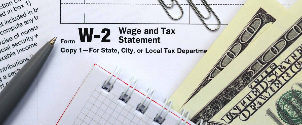 The pen, notebook and dollar bills is lies on the tax form W-2 W