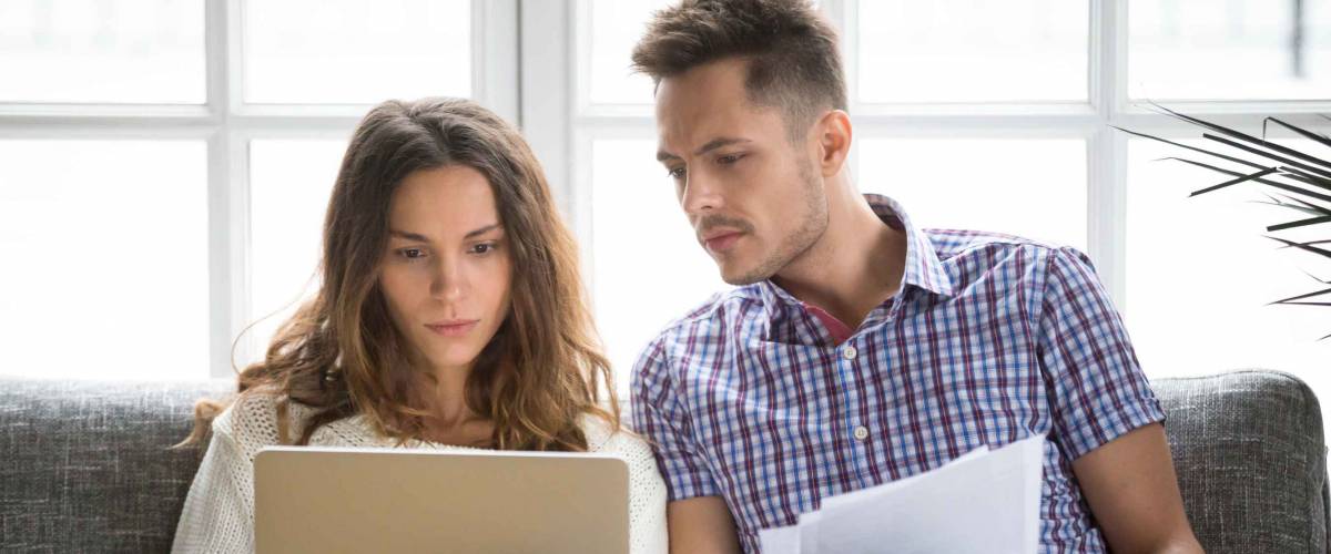 Man and woman sitting on couch, looking at laptop and papers