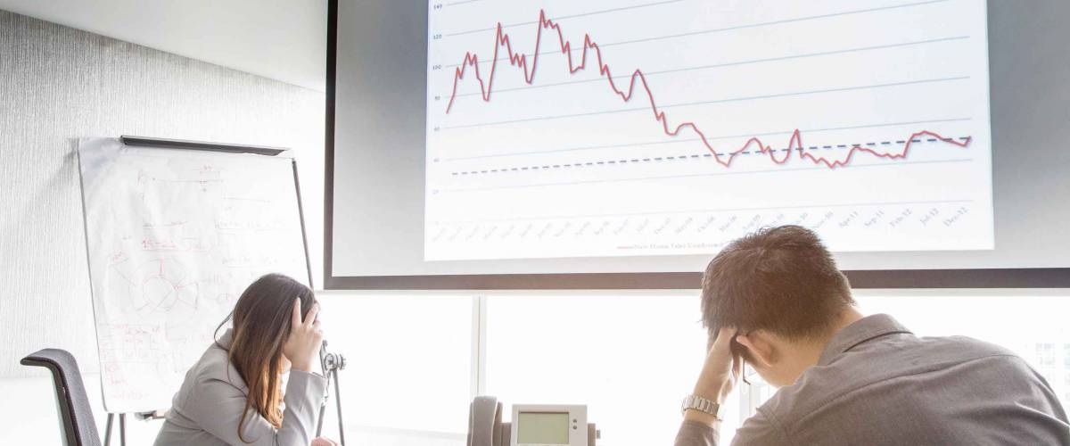 Serious and fail business man and woman in meeting room with negative graph on screen. They are waiting consultant form conference telephone
