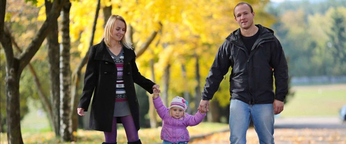 Man and woman holding hands with little girl between them, walking outside in the fall
