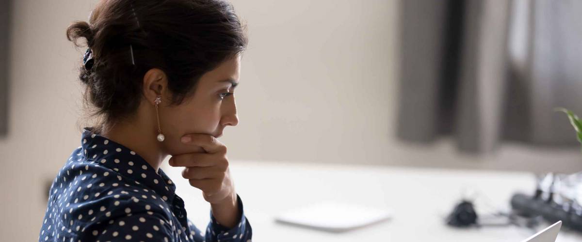 Young woman sitting at a desk, looking thoughtful and holding her chin with hand