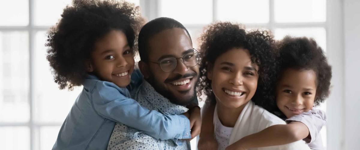 Smiling happy family facing camera, daughters on the back of both mom and dad