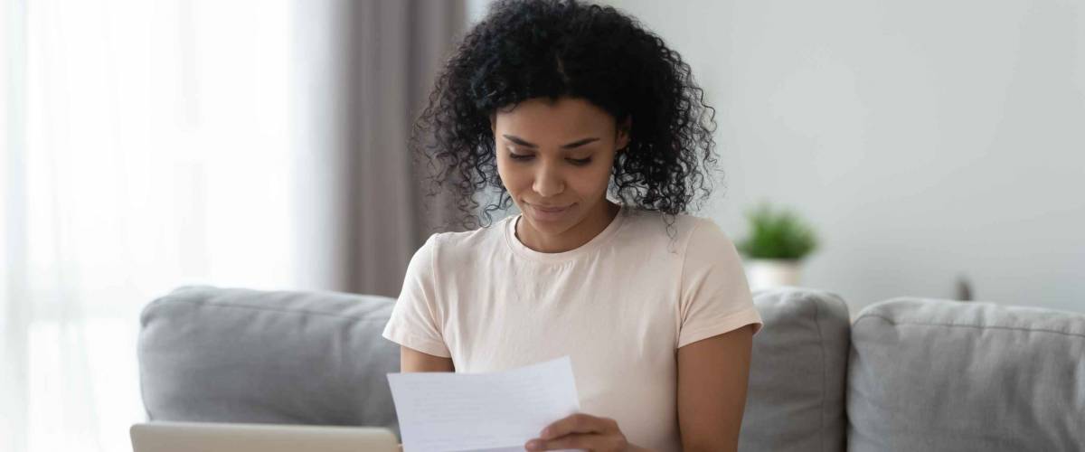 Smiling young woman looking at piece of paper while sitting on the couch