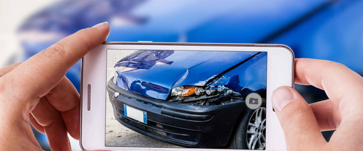 a woman using a smart phone to take a photo of the damage to her car caused by a car crash