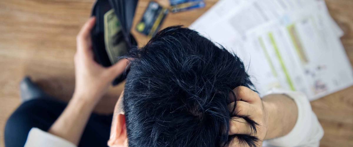 Top view of stressed young man holding wallet with money and looking at bills on the ground