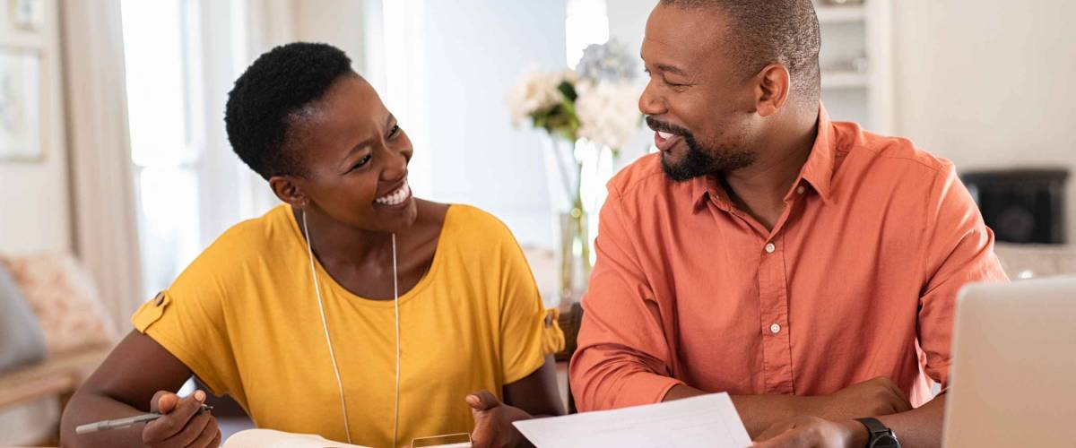 Happy looking couple sitting at kitchen table and looking at each other while holding bills