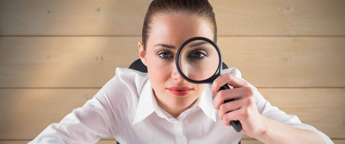 Businesswoman typing and looking through magnifying glass against bleached wooden planks background