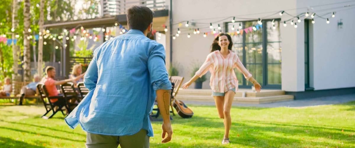 Beautiful Young Girl Runs Toward Her Boyfriend to Catche Him and Embrace. Two Young People in the Backyard of a Garden on a Hot Summer Day.