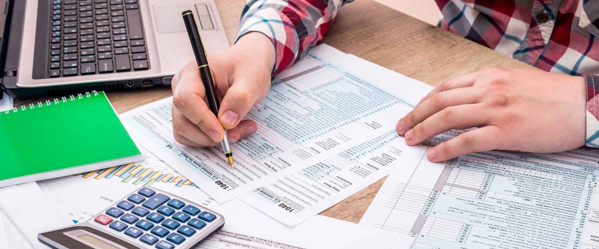 Man filling out 1040 tax form with help laptop caluclator and note at office desk