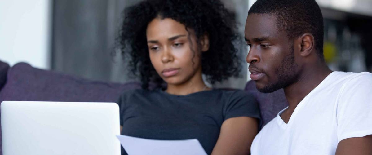 Serious looking couple sit on couch and look at laptop together
