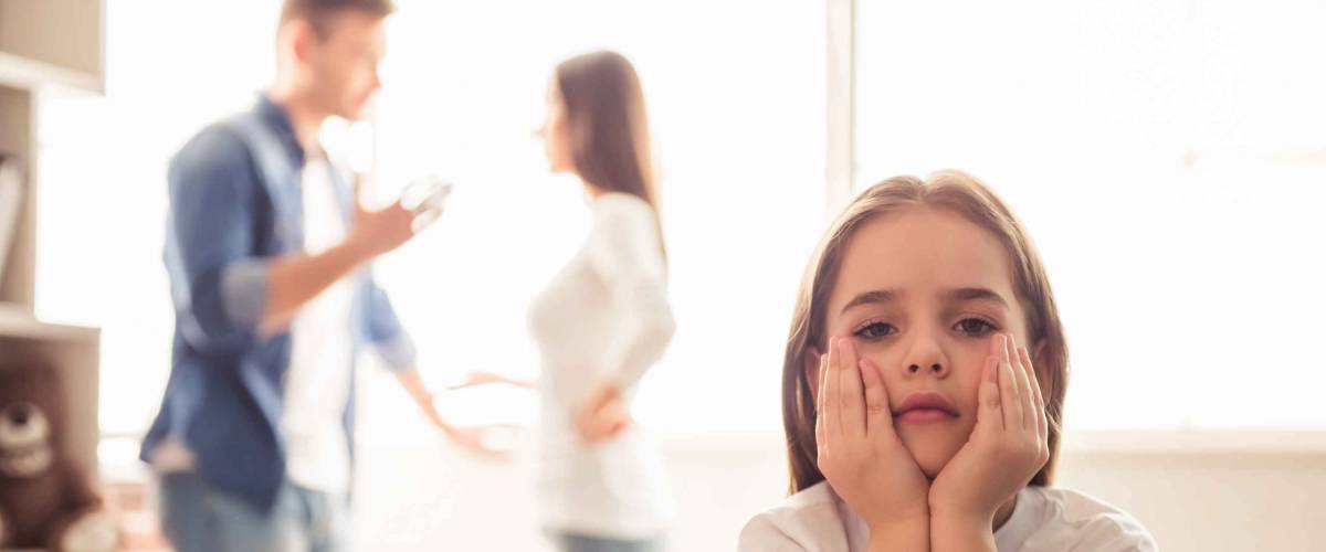 Sad little girl is looking at camera while her parents are arguing in the background