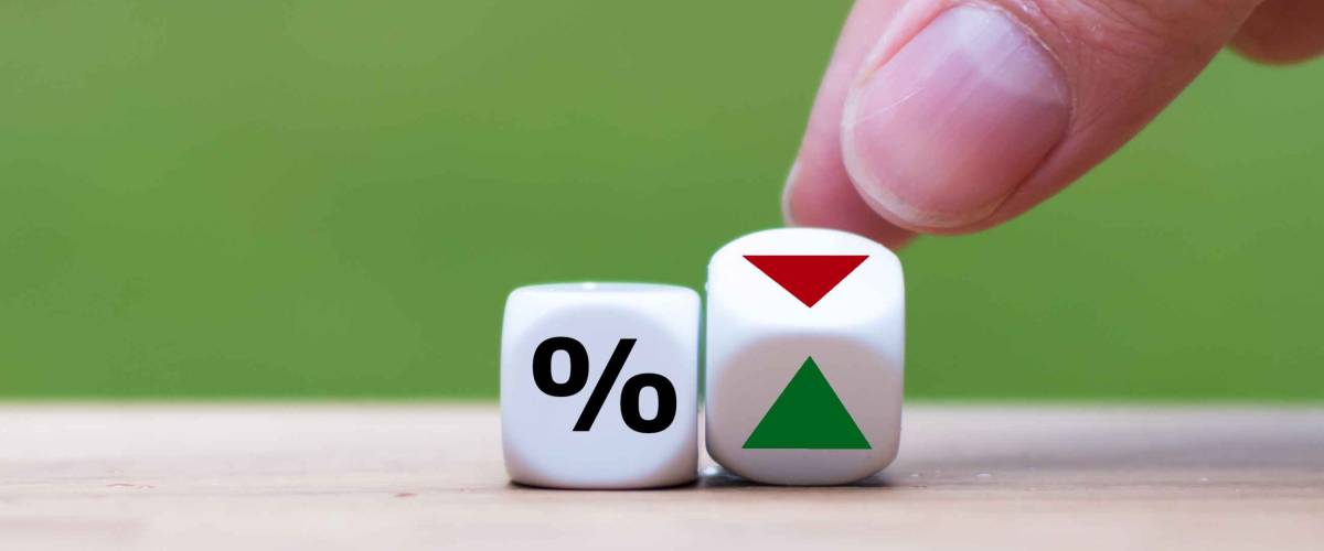 Hand is turning a dice and changes the direction of an arrow symbolizing that the interest rates are going down (or vice versa)