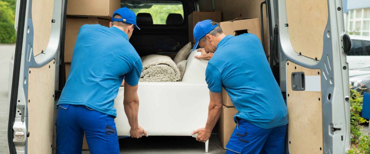Two Male Workers In Blue Uniform Adjusting Sofa In Truck