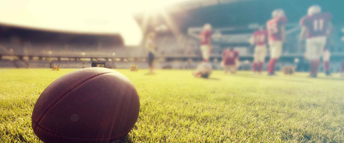 Close up of an american football on the field, players in the background