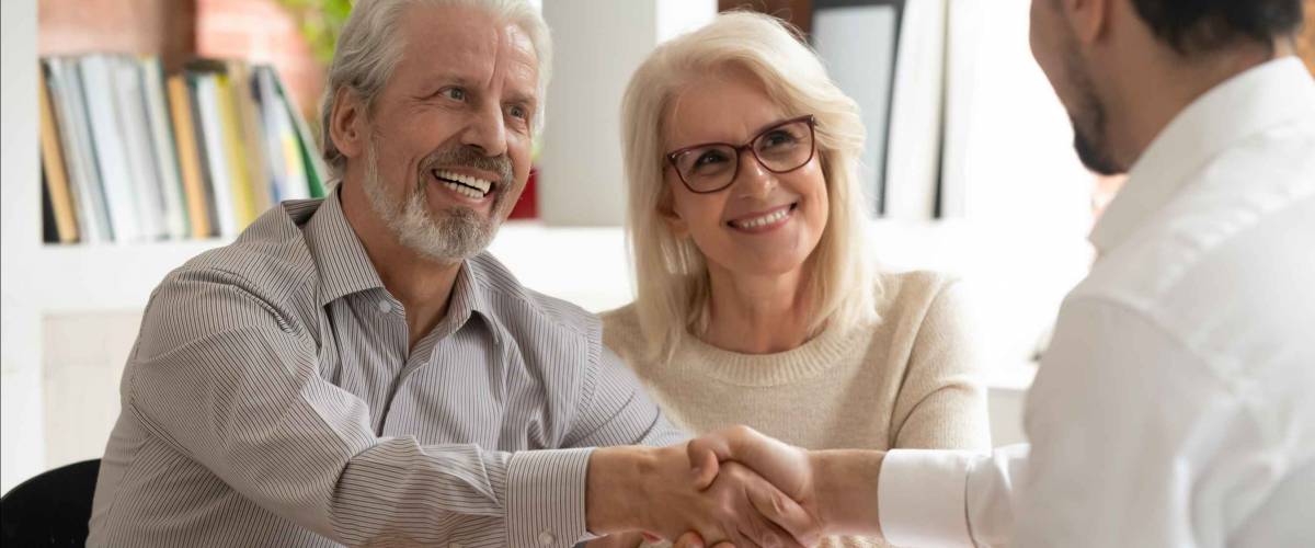 Smiling senior couple, man shaking hands with a young man sitting across a table