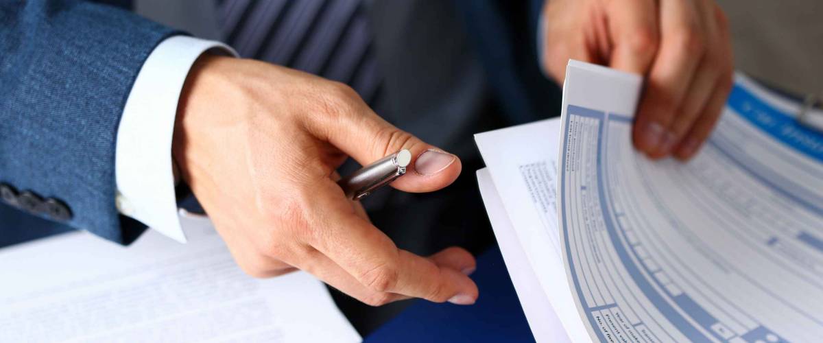 Close up of man in suit shuffling through insurance forms clipped to pad