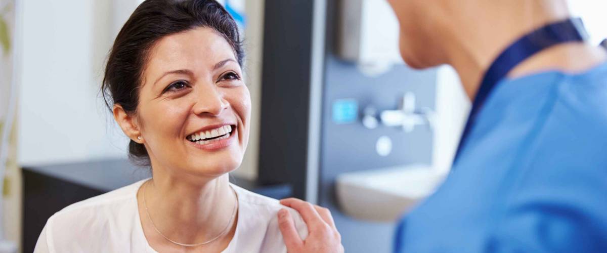 Female Patient Being Reassured By Doctor In Hospital Room