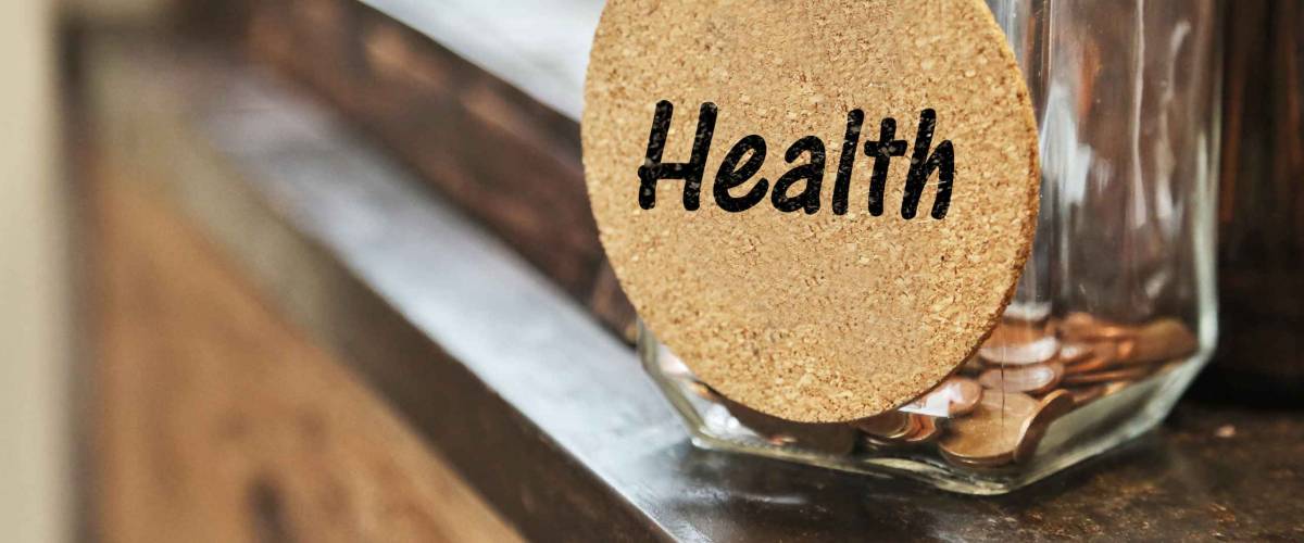 Vintage retro glass jar with hemp rope tie health tag and few coins inside on wood counter concept of save money for health care