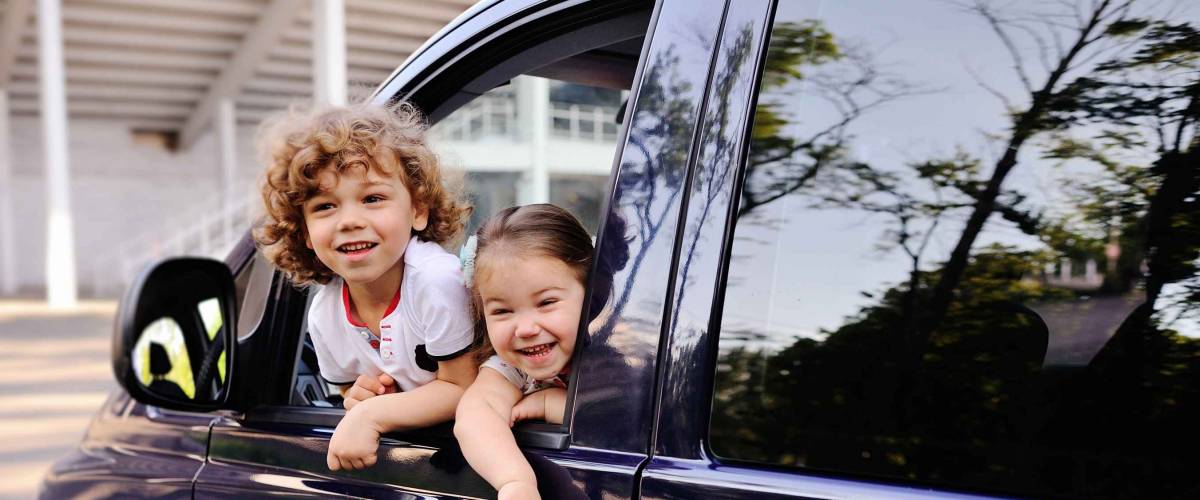 two little kids hang out window of minivan