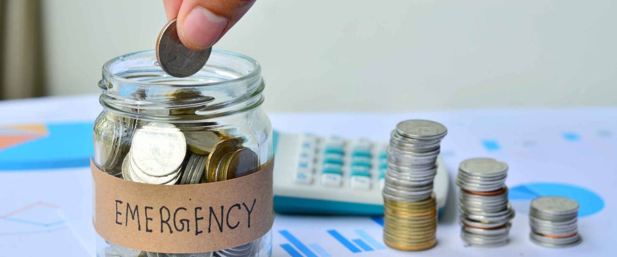Person dropping coin into full jar that says EMERGENCY with coins stacked beside it