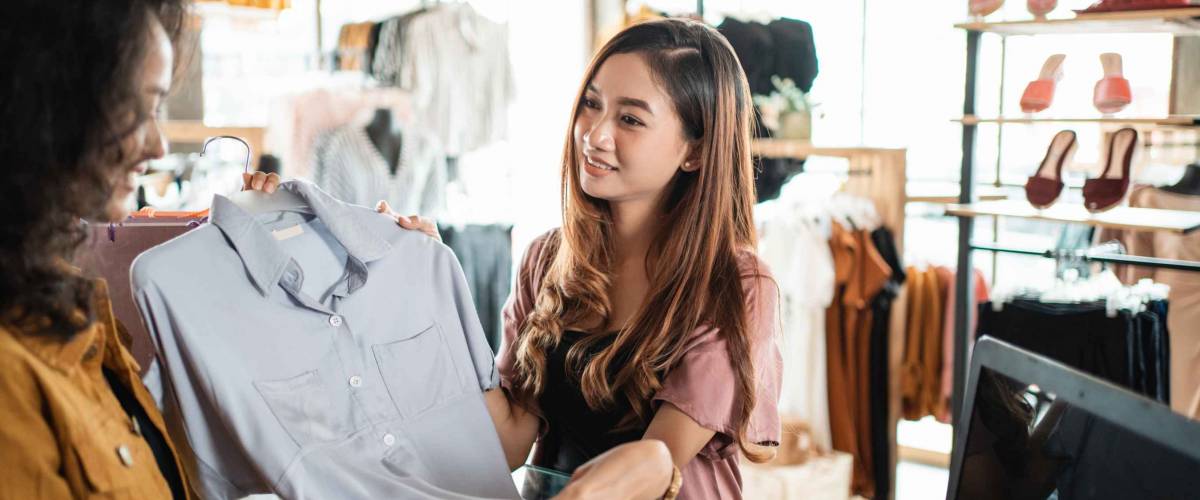 woman at a shop counter handing over shirt to return to store employee