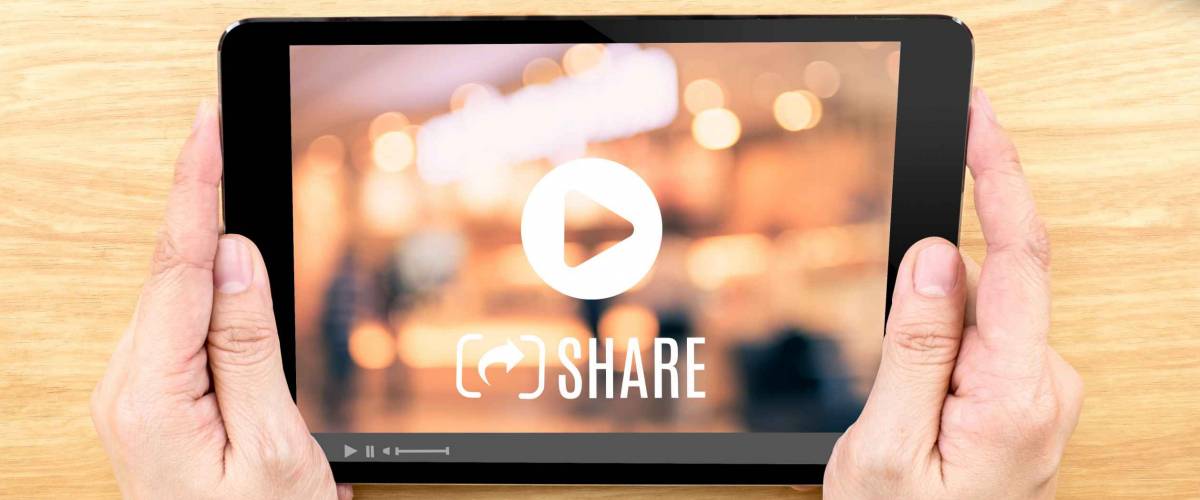 Hand holding tablet with Video sharing on screen on wood table