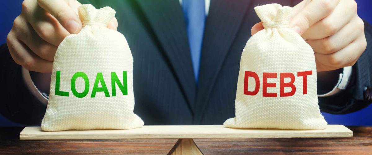 A businessman holds bags with a loan and debt on scales.
