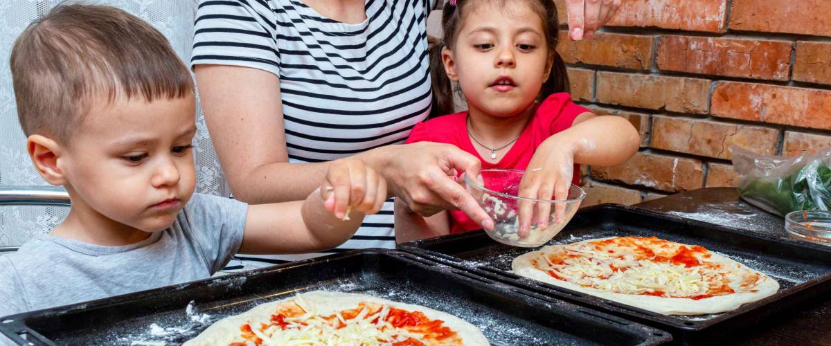 little boy and girl helping mom make pizza at home