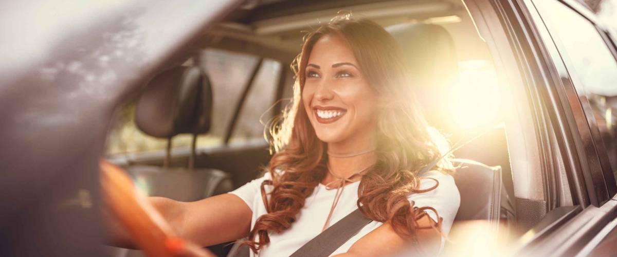 Beautiful young happy smiling woman driving her new car at sunset.