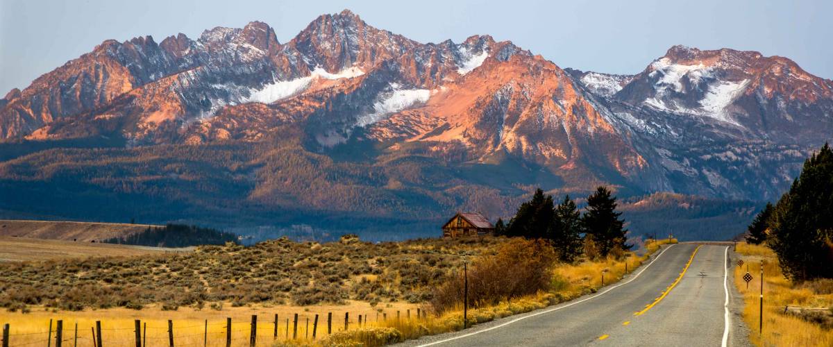 The Sawtooth mountains and a log cabin at sunrise and highway 75 leading to Stanley, Idaho.