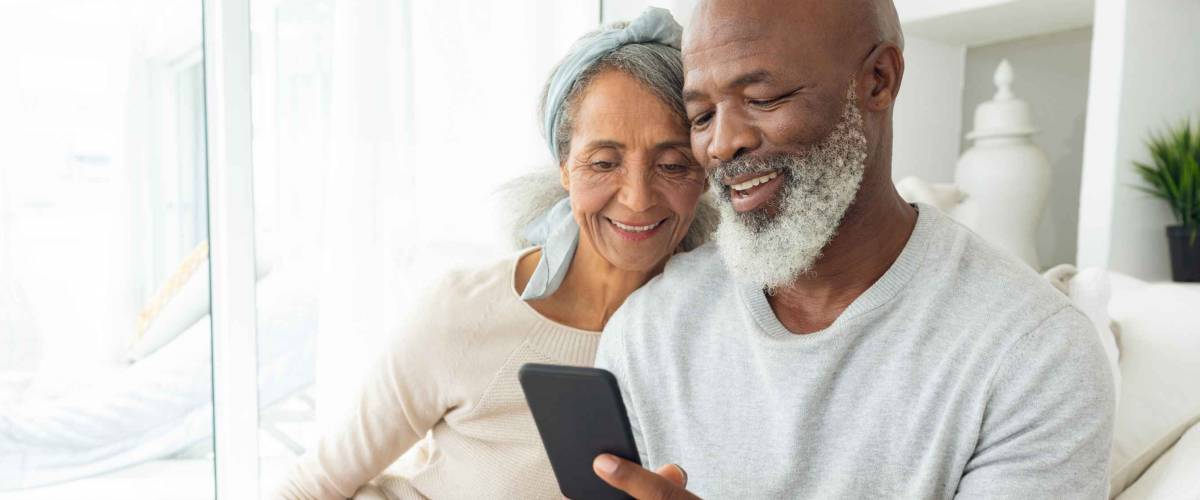 Older couple sitting on a couch, smiling, looking at a smartphone