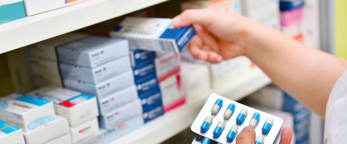 Pharmacist holding medicine box and capsule pack in pharmacy drugstore.
