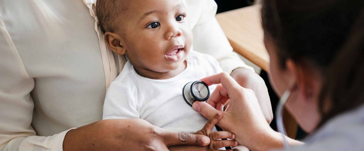 Doctor seen from behind using stethoscope on baby