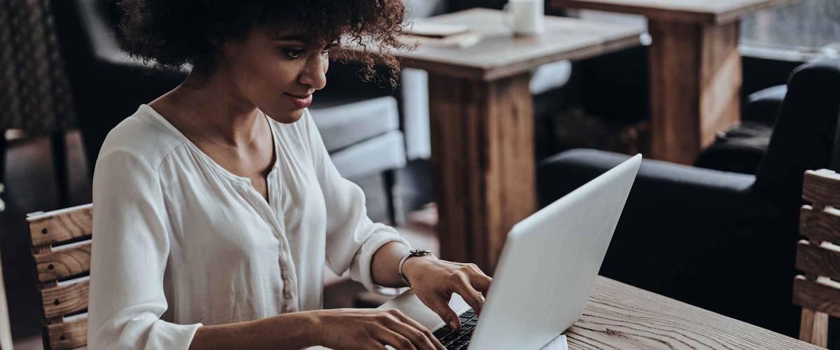 Young woman sitting at table at cafe, using laptop